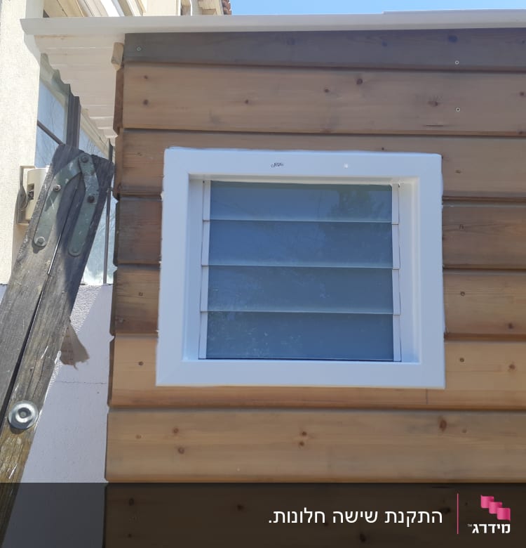 חלון עם תריסי אלומיניום על קיר עץ